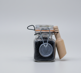 Small glass jar with black powder and a wooden scoop on a light gray background