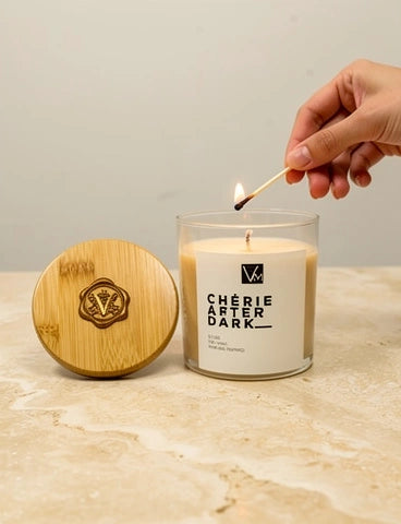 Candle labeled 'Chérie After Dark' being lit with a wooden lid on a marble surface.
