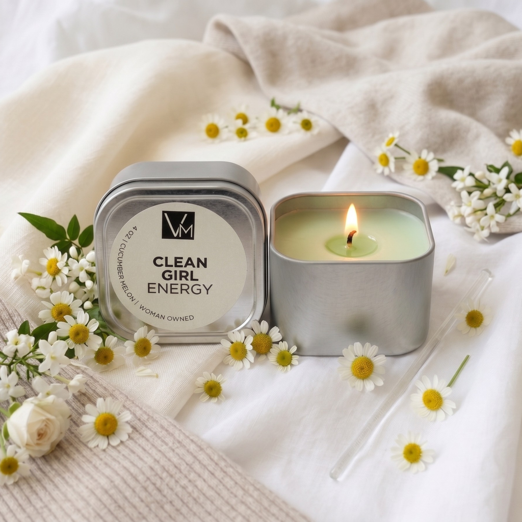 Candle in a tin labeled 'Clean Girl Energy' surrounded by flowers on a soft fabric background