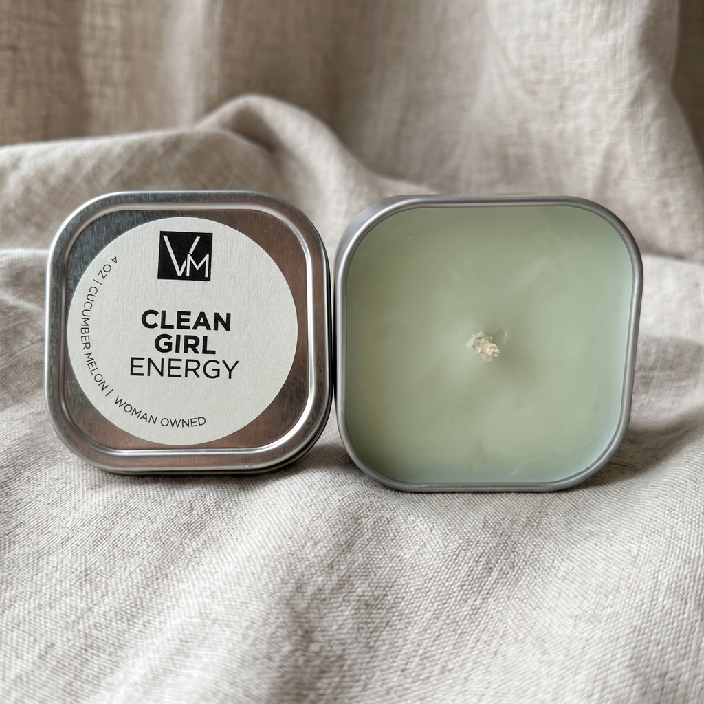 Candle in a tin labeled 'Clean Girl Energy' on a beige fabric background