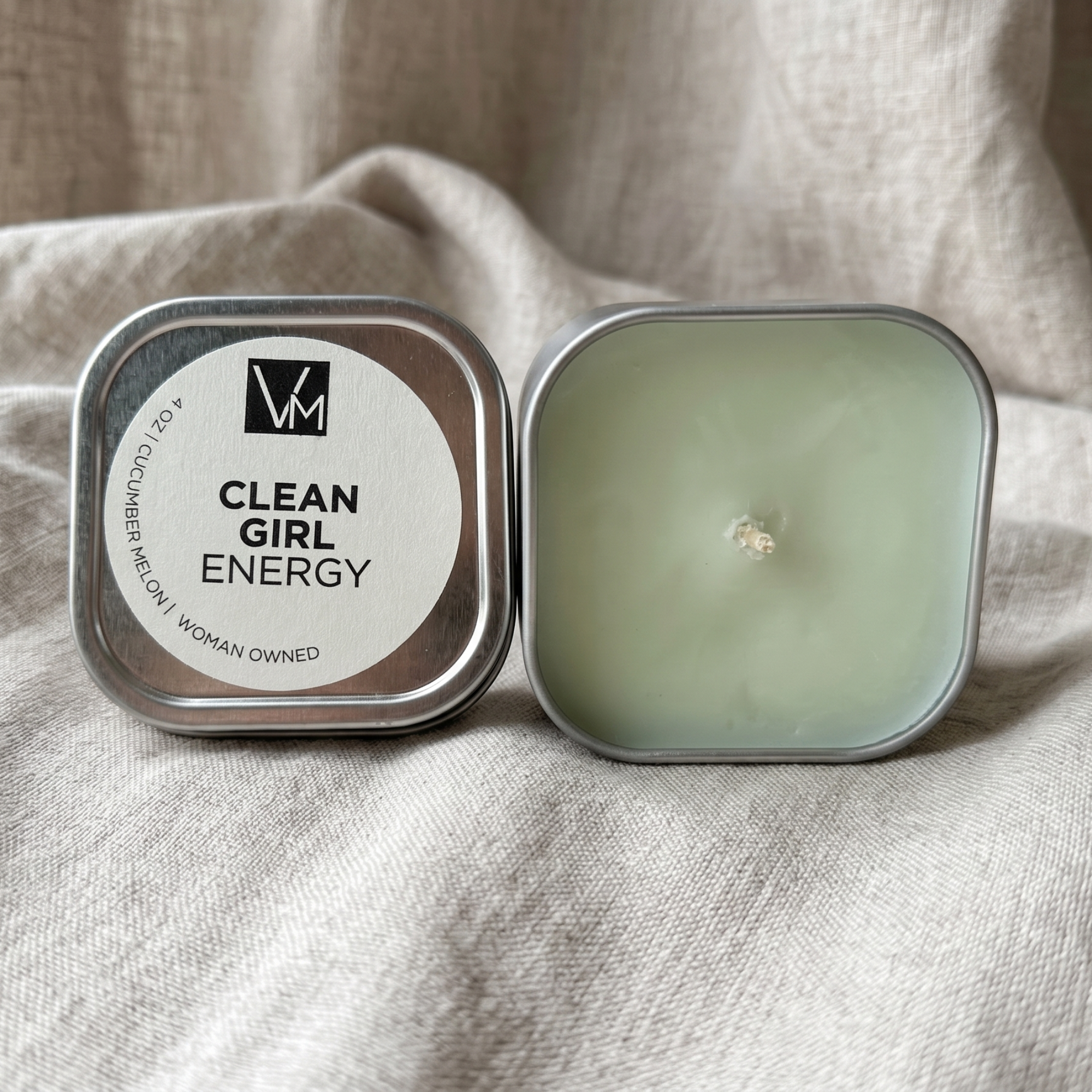 Candle in a tin labeled 'Clean Girl Energy' on a beige fabric background